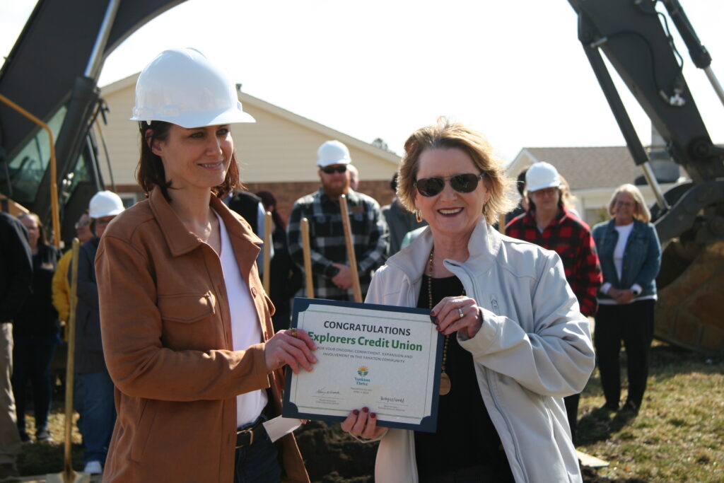 Credit union executives wearing hard hats and holding certificates with construction in the background.