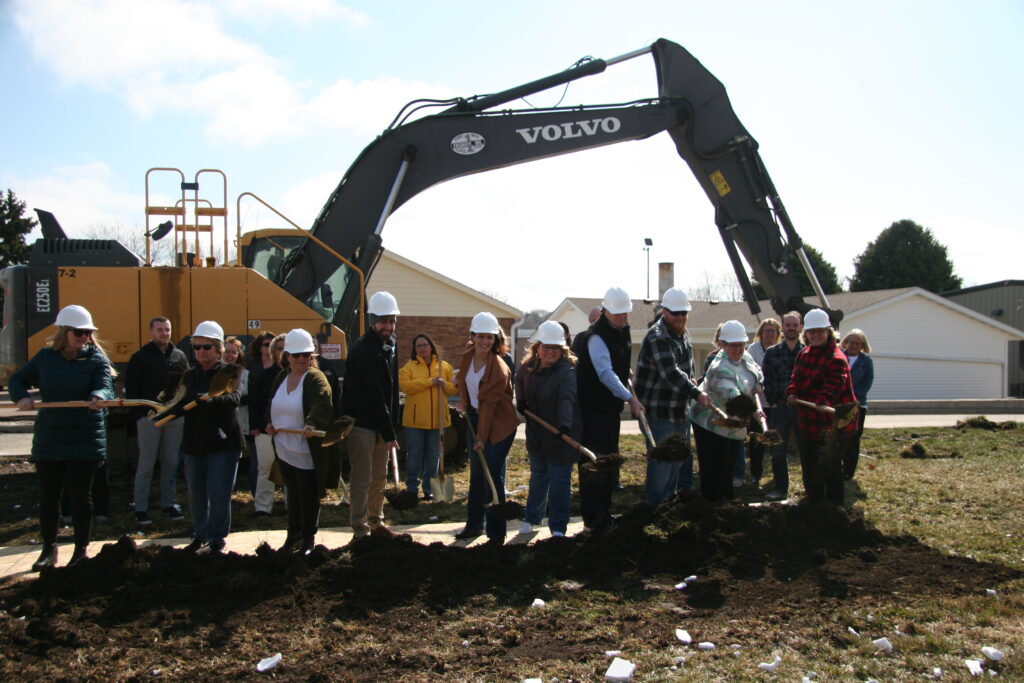 Group of people posing for groundbreaking by construction equipment.