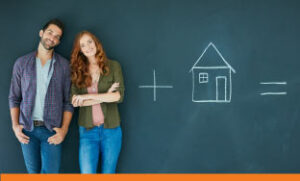 Couple standing in front of a chalkboard with chalk drawing of a house.