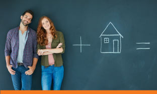 Couple standing in front of a chalkboard with chalk drawing of a house.